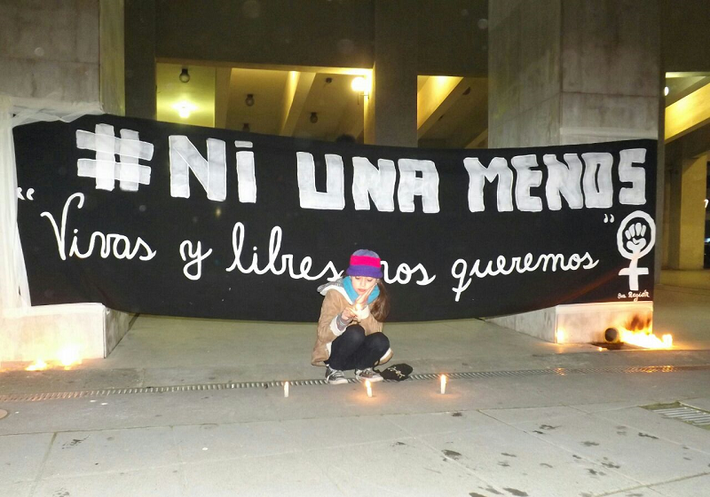 Pancarta negra con letras blancas que dice: #NiUnaMenos, Vivas y libres los queremos.