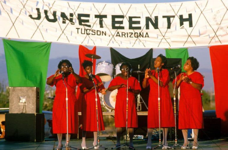 Cinco cantantes afroamericanas celebrando Juneteenth con alegre canción.